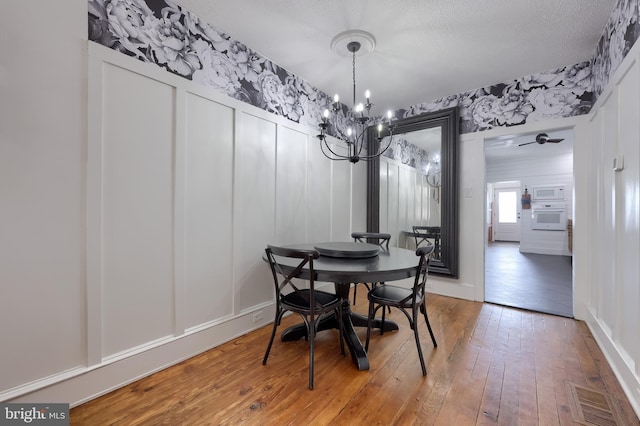 dining room featuring hardwood / wood-style flooring, a chandelier, wallpapered walls, a decorative wall, and a textured ceiling