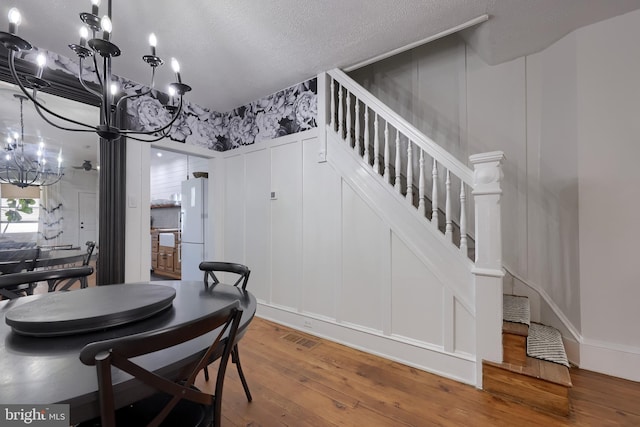 dining area with a chandelier, a decorative wall, wood-type flooring, stairs, and a textured ceiling
