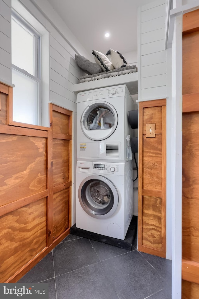 laundry room featuring estacked washer and dryer and dark tile patterned floors