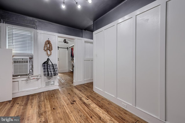 interior space featuring wood-type flooring, cooling unit, a decorative wall, and a ceiling fan
