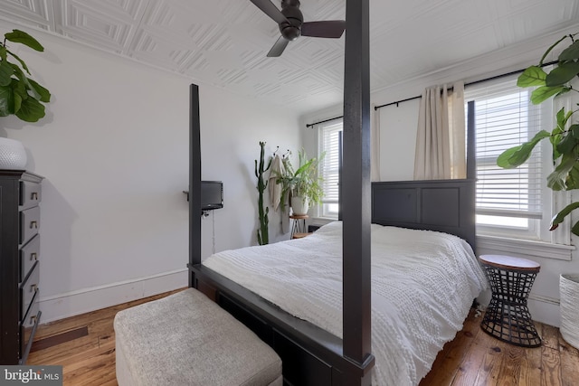 bedroom featuring an ornate ceiling, hardwood / wood-style floors, baseboards, and a ceiling fan
