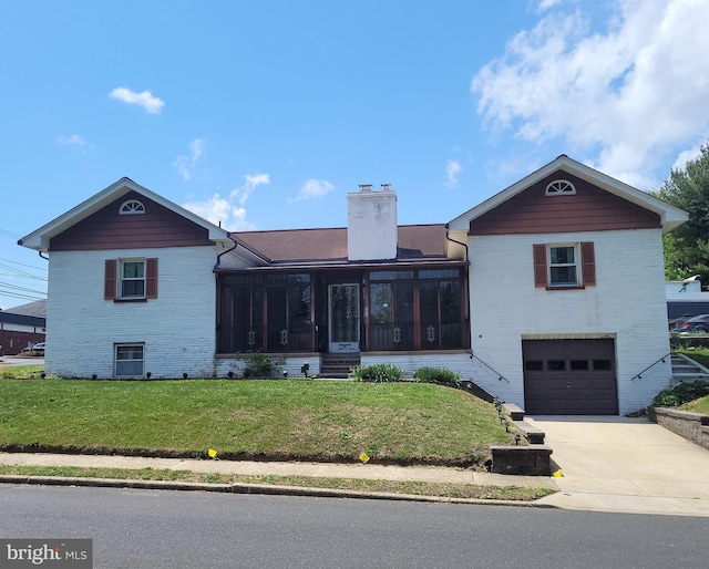 view of front of home with a sunroom, a chimney, a front yard, a garage, and brick siding