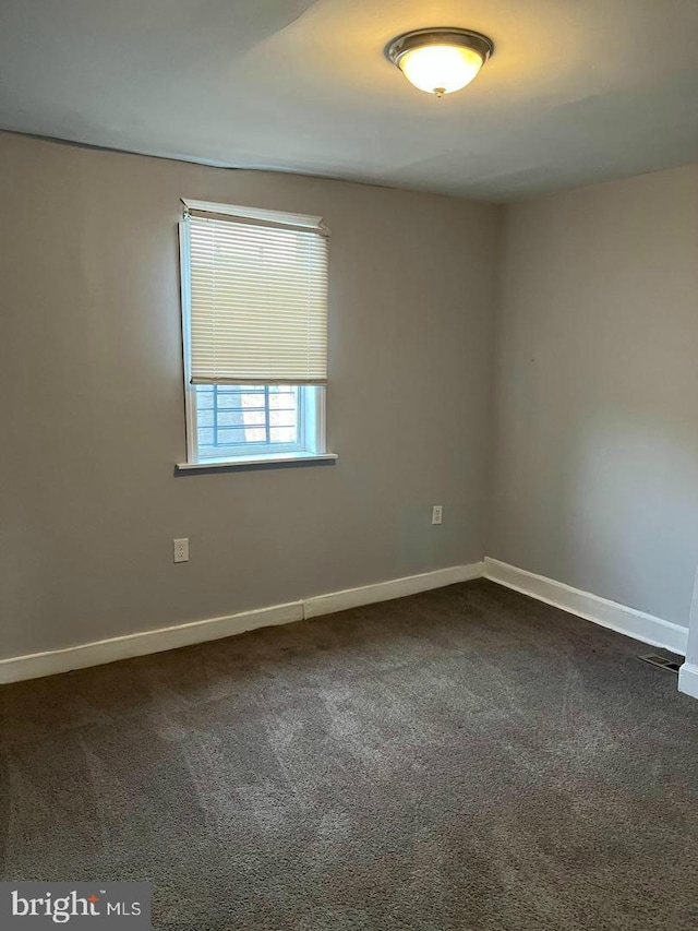 empty room featuring dark colored carpet and baseboards