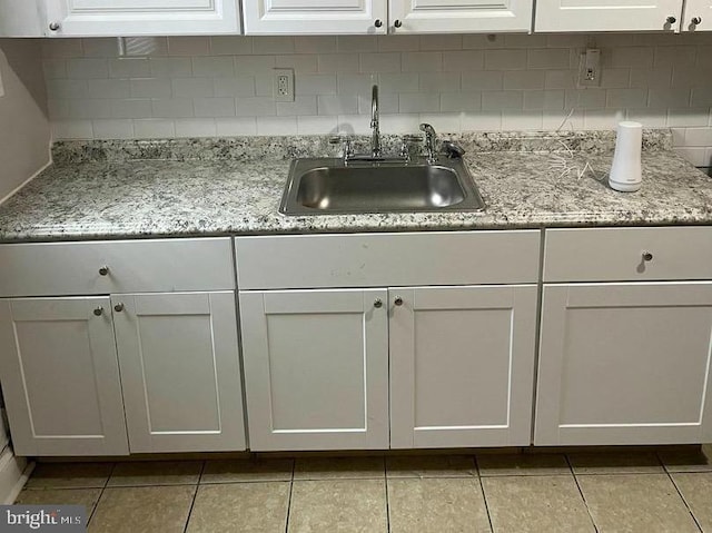 kitchen with a sink, light tile patterned floors, white cabinets, and backsplash