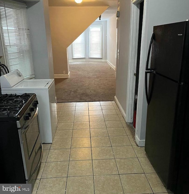 clothes washing area featuring light colored carpet, light tile patterned floors, baseboards, and washer / dryer