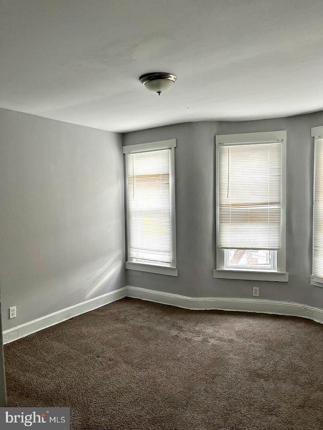 spare room with dark carpet and baseboards