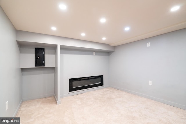 finished basement featuring light colored carpet, baseboards, a glass covered fireplace, and recessed lighting
