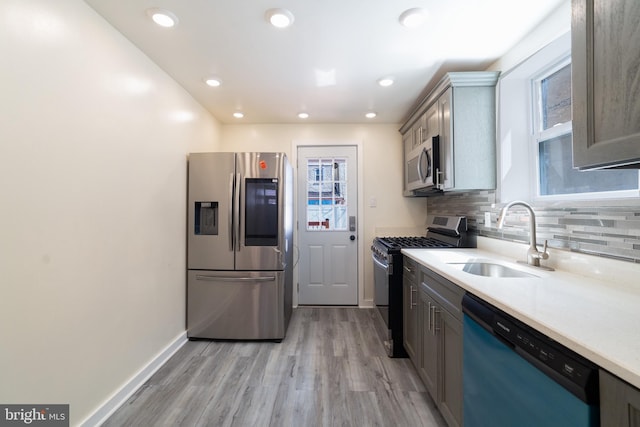 kitchen with light wood finished floors, a sink, stainless steel appliances, baseboards, and light countertops