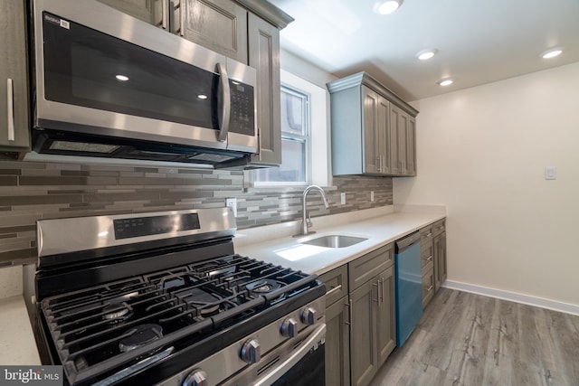 kitchen with a sink, stainless steel appliances, tasteful backsplash, light countertops, and gray cabinetry