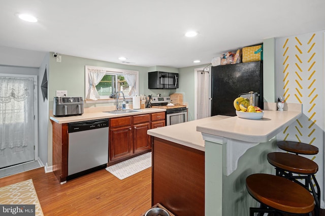 kitchen with stainless steel appliances, a sink, a breakfast bar, light wood finished floors, and light countertops
