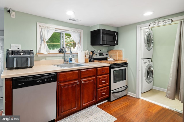 kitchen featuring stainless steel appliances, stacked washer / dryer, a sink, light countertops, and wood finished floors