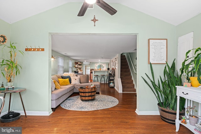 living area featuring vaulted ceiling, wood finished floors, a ceiling fan, baseboards, and stairway