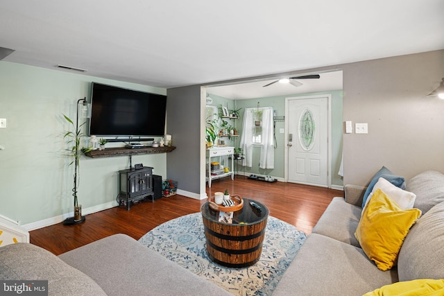 living room featuring a wood stove, wood finished floors, ceiling fan, and baseboards