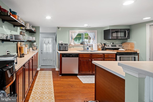 kitchen featuring appliances with stainless steel finishes, a sink, open shelves, wood finished floors, and light countertops