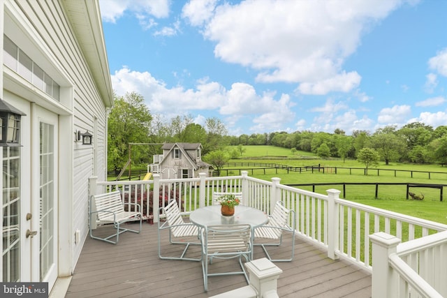 wooden deck featuring a view of countryside, an outdoor structure, outdoor dining space, and view of wooded area