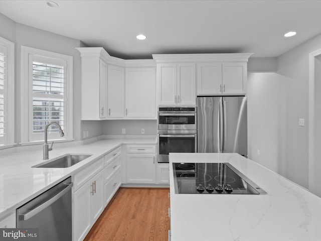 kitchen with appliances with stainless steel finishes, a sink, white cabinetry, recessed lighting, and light stone countertops