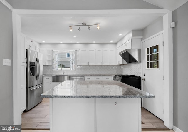 kitchen featuring appliances with stainless steel finishes, a sink, wall chimney range hood, white cabinetry, and a center island