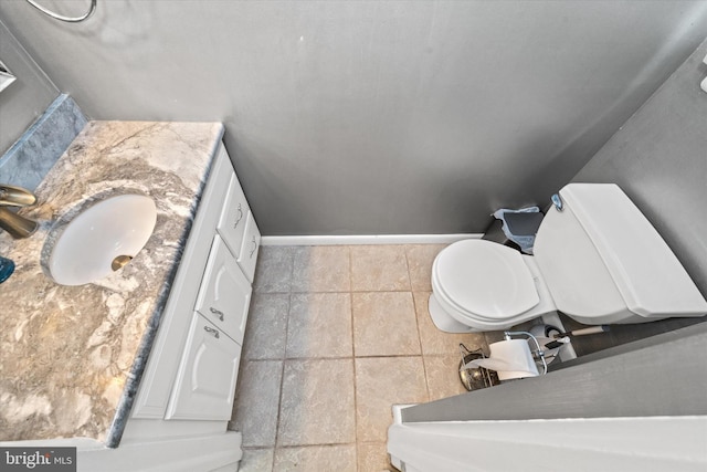 half bath with toilet, vanity, baseboards, and stone finish floors