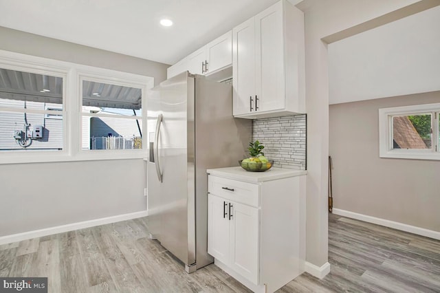 kitchen featuring stainless steel refrigerator with ice dispenser, white cabinetry, decorative backsplash, light wood-type flooring, and recessed lighting
