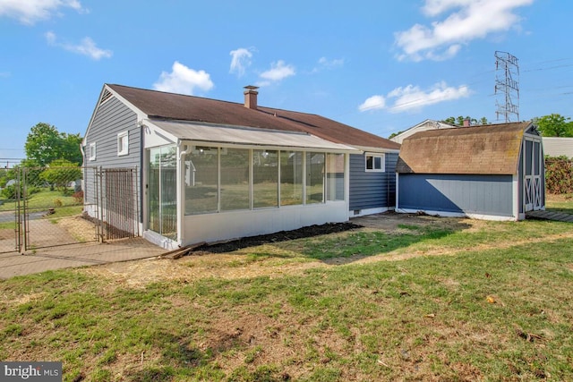 rear view of property featuring a storage shed, a sunroom, an outbuilding, and a gate