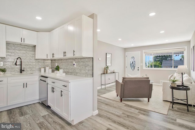 kitchen featuring a sink, dishwasher, white cabinetry, backsplash, and light countertops