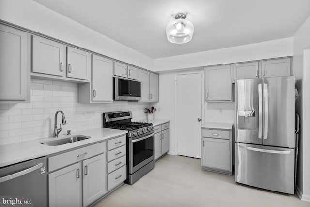 kitchen with stainless steel appliances, a sink, gray cabinets, light countertops, and tasteful backsplash