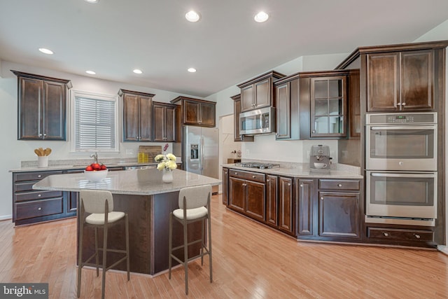 14762 Bell Tower Rd, Woodbridge, VA 22193 - kitchen with appliances with stainless steel finishes, dark brown cabinets, light wood finished floors, a kitchen bar, and recessed lighting