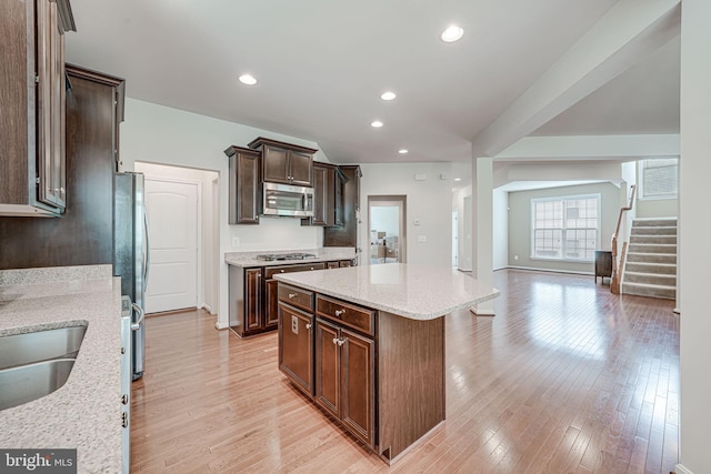 14762 Bell Tower Rd, Woodbridge, VA 22193 - kitchen with appliances with stainless steel finishes, a kitchen island, light wood-style flooring, light stone countertops, and dark brown cabinetry