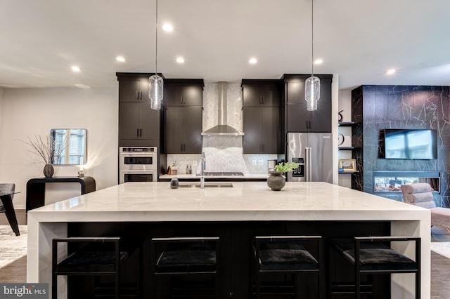 kitchen featuring wall chimney exhaust hood, appliances with stainless steel finishes, a large island, recessed lighting, and wood finished floors