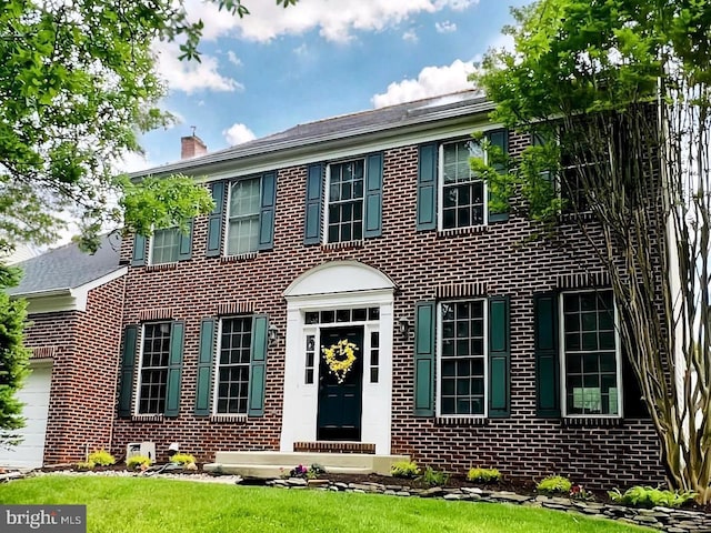 colonial-style house with brick siding, a chimney, an attached garage, and a front yard
