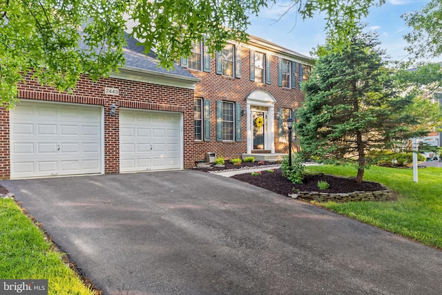view of front facade with brick siding, asphalt driveway, an attached garage, a front lawn, and roof with shingles