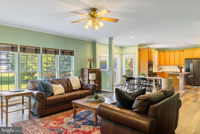 living room featuring a ceiling fan, plenty of natural light, light wood-style floors, recessed lighting, and ornamental molding