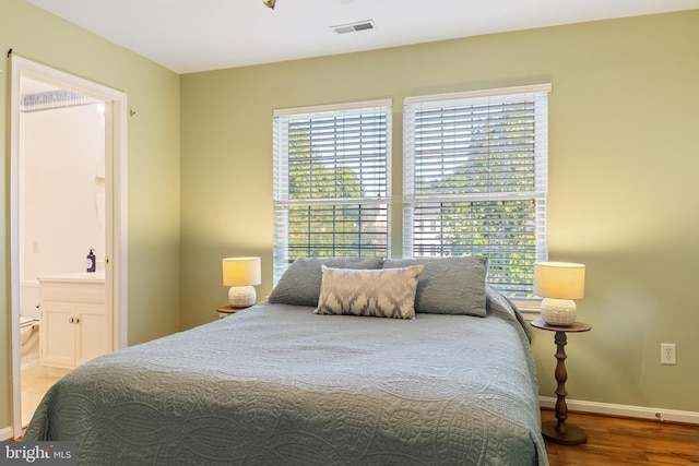 bedroom with wood finished floors, baseboards, and ensuite bath