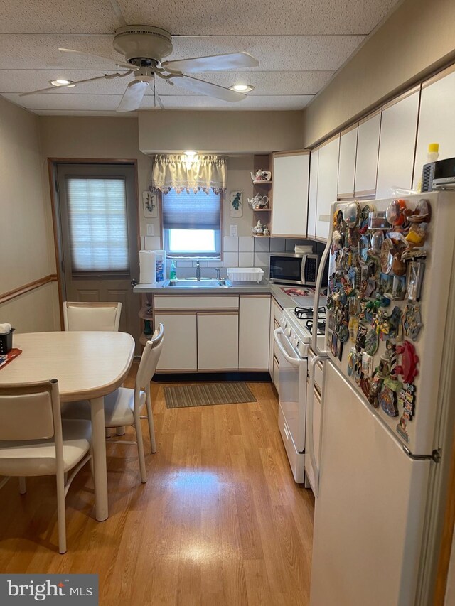 kitchen with white appliances, a sink, white cabinetry, a ceiling fan, and light wood-type flooring