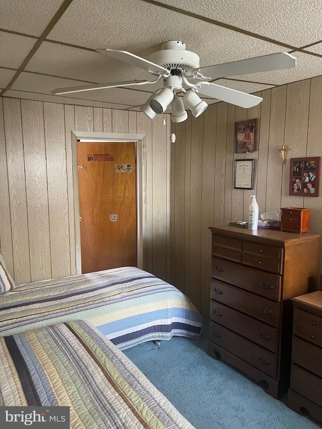 carpeted bedroom featuring wood walls and a ceiling fan