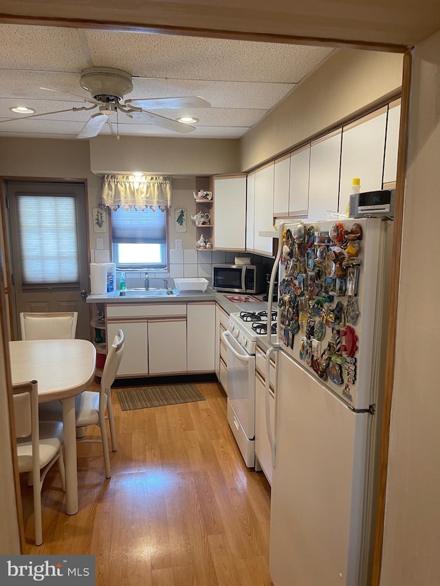 kitchen featuring white appliances, a sink, white cabinetry, light wood-type flooring, and a ceiling fan
