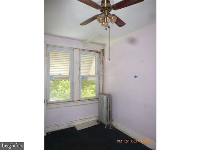 empty room with radiator, a ceiling fan, and baseboards