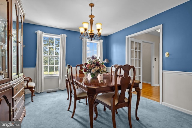 dining space featuring a chandelier, light colored carpet, and baseboards