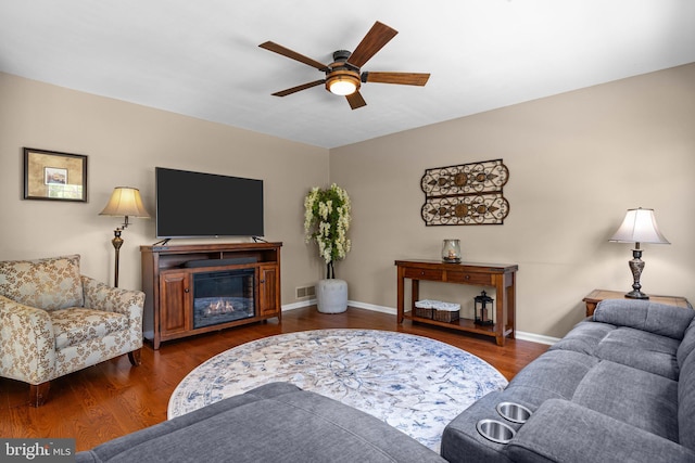 living area with a ceiling fan, a glass covered fireplace, wood finished floors, and baseboards