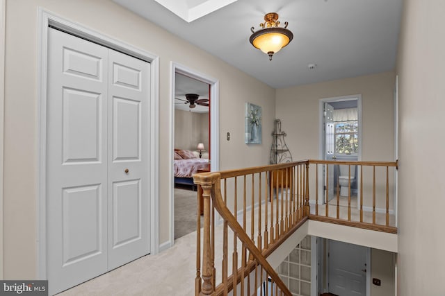 corridor with light colored carpet and an upstairs landing