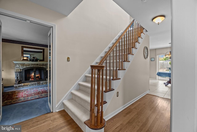 stairs with wood finished floors, a stone fireplace, and baseboards