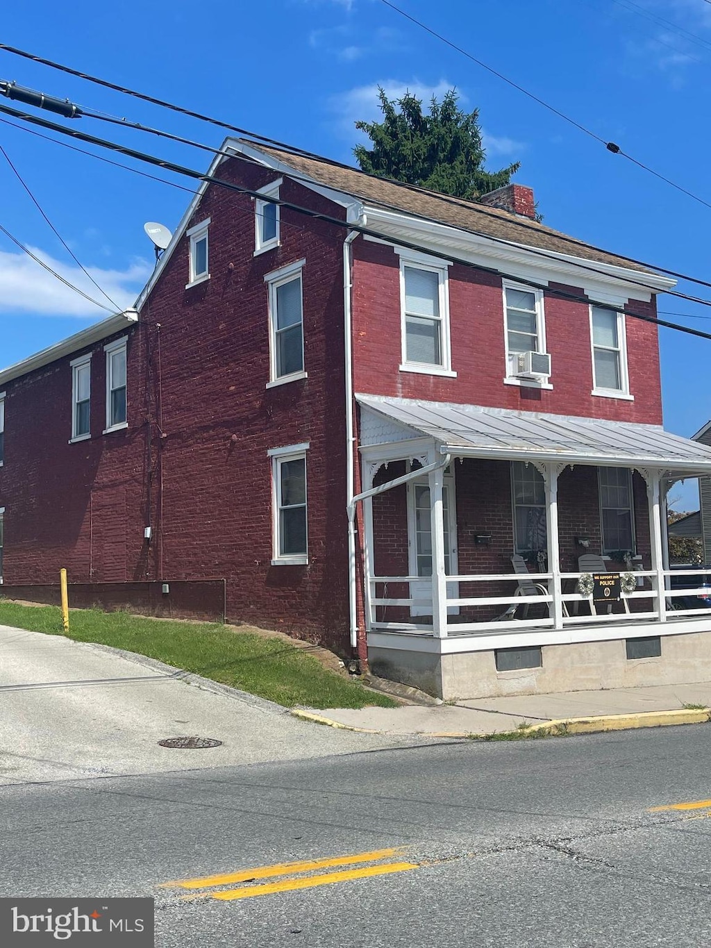 view of front facade with a porch, brick siding, a chimney, and cooling unit