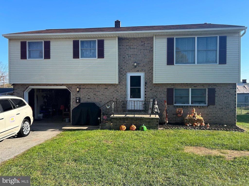 split foyer home featuring concrete driveway, an attached garage, brick siding, and a front lawn