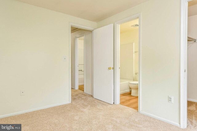 unfurnished bedroom with carpet, a spacious closet, baseboards, a closet, and ensuite bathroom