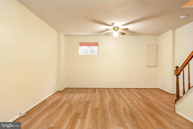 spare room featuring a ceiling fan, stairs, light wood-style flooring, and baseboards