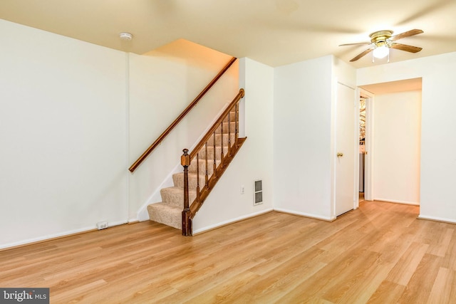 unfurnished living room with ceiling fan, light wood finished floors, stairway, and baseboards