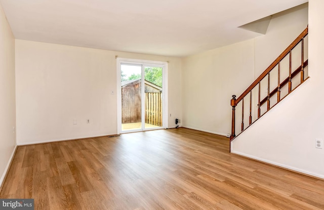 unfurnished living room with wood finished floors, stairway, and baseboards
