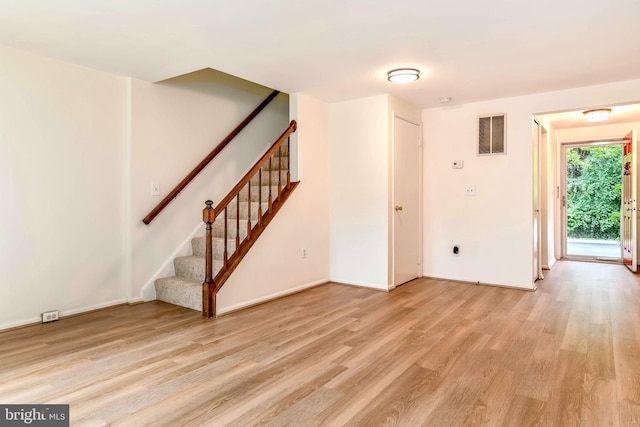 unfurnished living room with light wood-type flooring, stairs, and baseboards