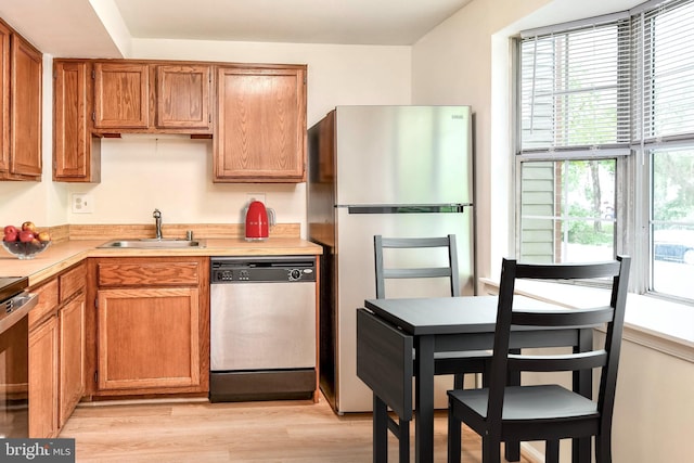 kitchen with appliances with stainless steel finishes, a sink, light countertops, light wood finished floors, and brown cabinetry