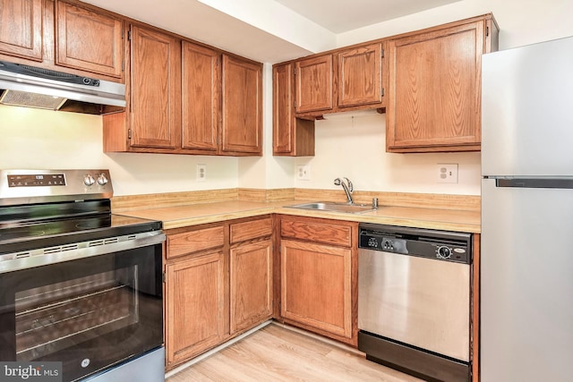 kitchen featuring stainless steel appliances, under cabinet range hood, a sink, light countertops, and light wood finished floors